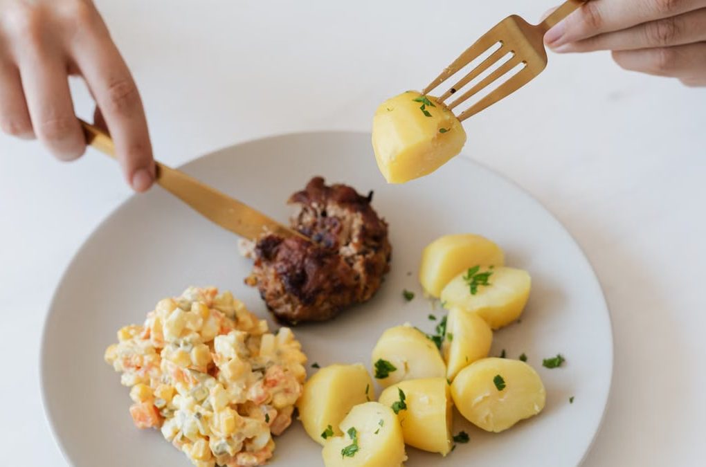From above of crop anonymous person with cutleries eating delicious fried cutlet and hot boiled potatoes with parsley garnished with nutritious Russian salad