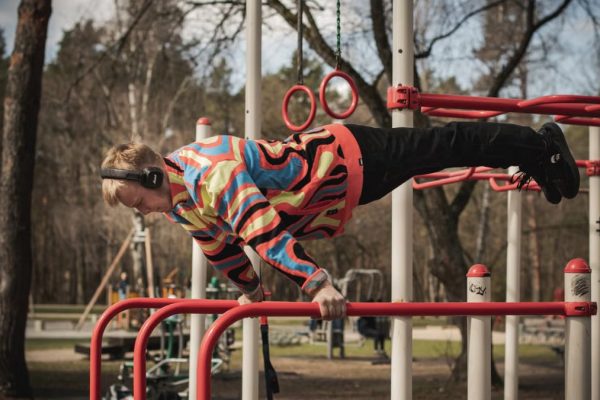 Young adult man exercises on outdoor gym bars in a colorful outfit in Vilnius, Lithuania.