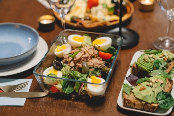 Elegant dining setup with fresh salad, avocado toast, and wine glasses on a wooden table.